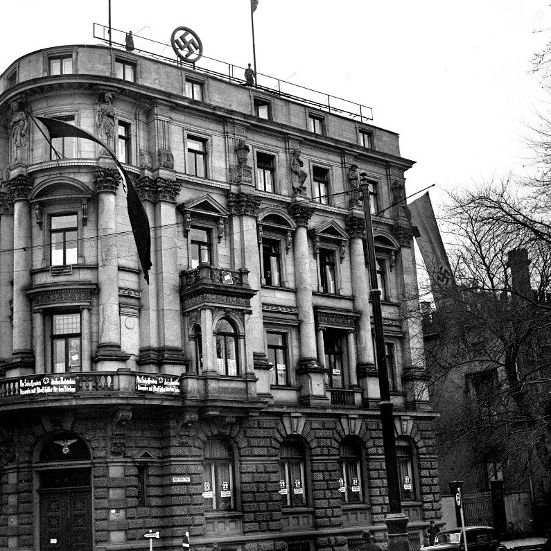 Hannover: Ehemaliges Haus des Fabrikarbeiterverbandes, Adolf-Hitler-Platz 3, (vor 1933 Rathenauplatz, nach 1945 Rathenaustraße, jetzt An der Börse 3). Gebäude mit Hakenkreuzfahnen und Emblem auf dem Dach. Banner: “ Die Schaffenden dieses Betriebes kämpfen mit Adolf Hitler für den Frieden“. Foto von Wilhelm Hauschild, 1933. HAZ-Hauschild-Archiv im Historischen Museum Hannover