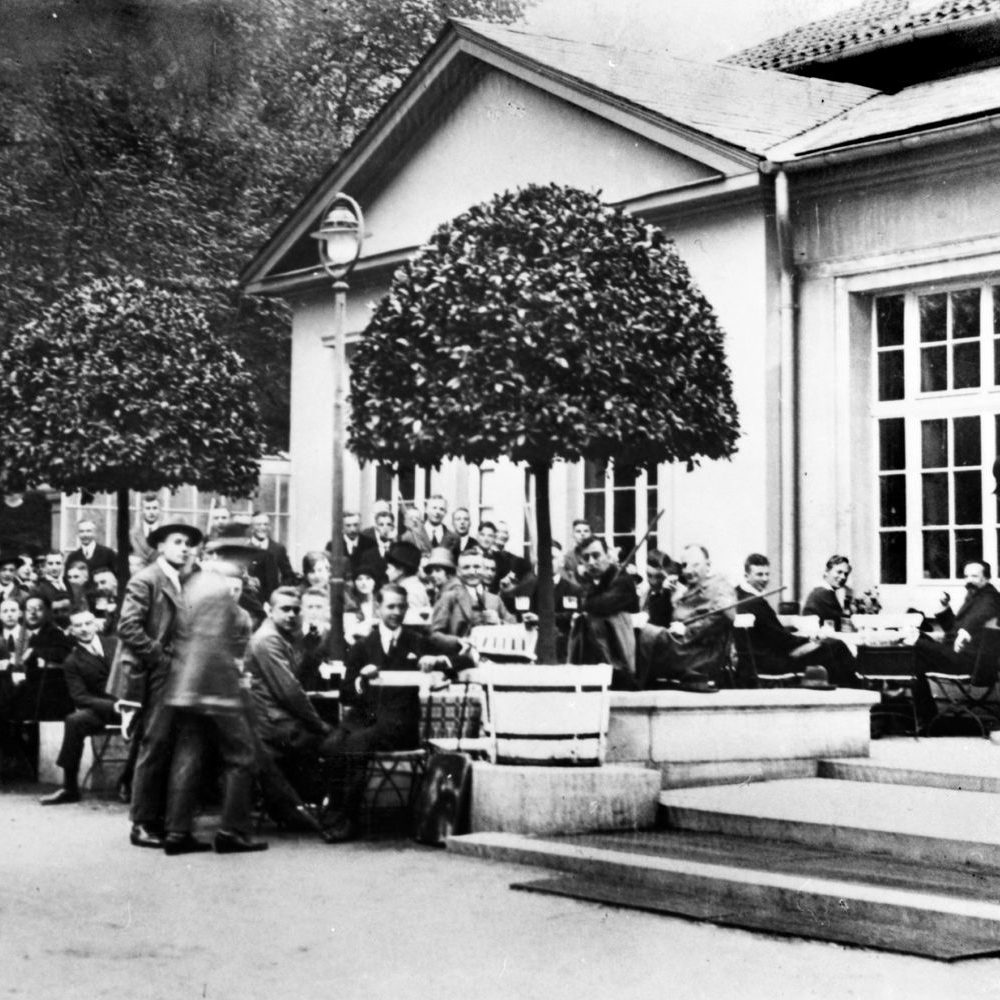 Hannover: Theodor Lessing (rechts im Bild sitzend) in einem Café im Georgengarten nahe der Technischen Universität, vor ihm teils mit Stangen bewaffnete Studenten, 3. Mai 1926. Bildarchiv Historisches Museum Hannover