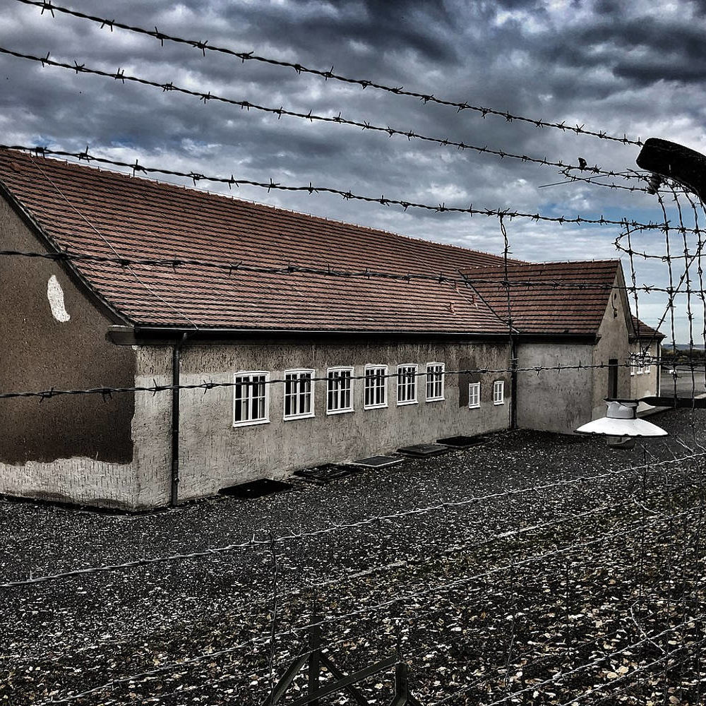 Ehemalige Häftlingskantine des KZ Buchenwald mit Blick durch den Sicherheitszaun, 2019. "Seit 1941 betrieb die SS eine Verkaufseinrichtung im Lager, die sogenannte Häftlingskantine, um Unterstützungsgelder von Angehörigen der Häftlinge abzuschöpfen." (Text Gedenkstätte Buchenwald) Foto TobiToaster. Wikimedia Commons